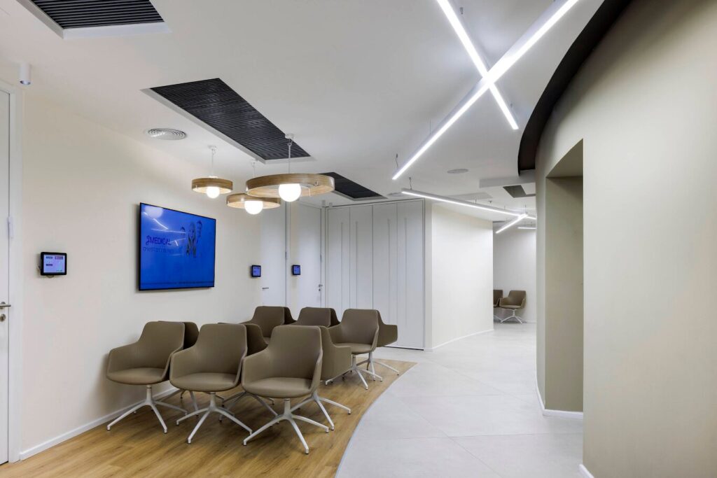 אזור ההמתנה במרפאת JMEDICAL עם מסך מידע ומסכים ליד חדרי הרופאים